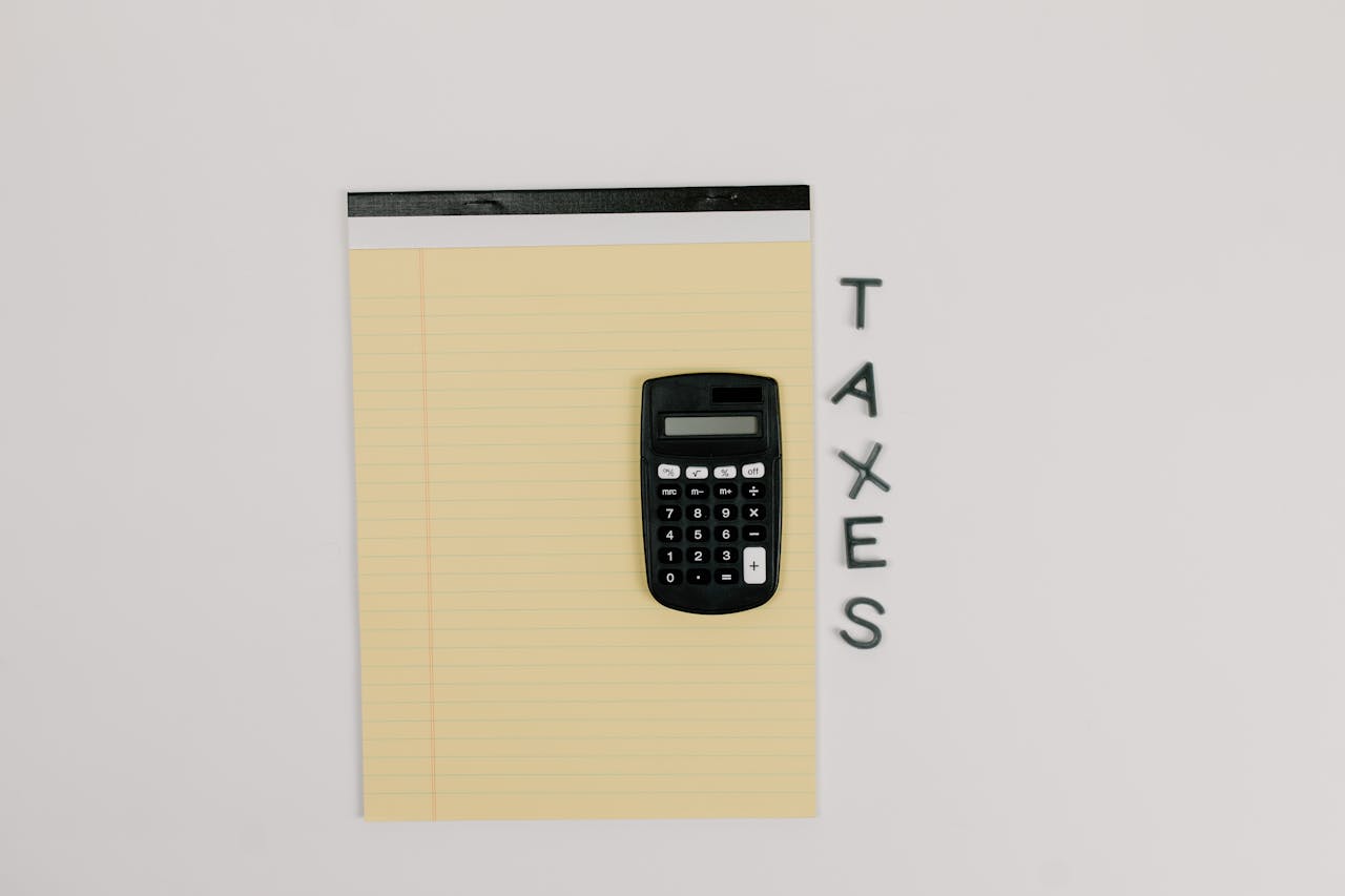Top-down view of a calculator on a yellow notepad with TAXES spelled out beside.